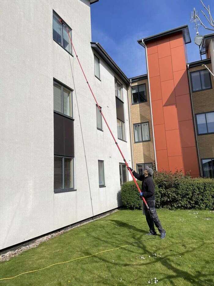 Window cleaner using a long pole on windows of a modern residential building