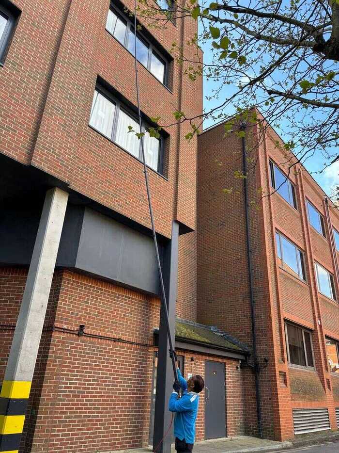 Cleaner using a long pole to clean windows on a multi-storey brick building