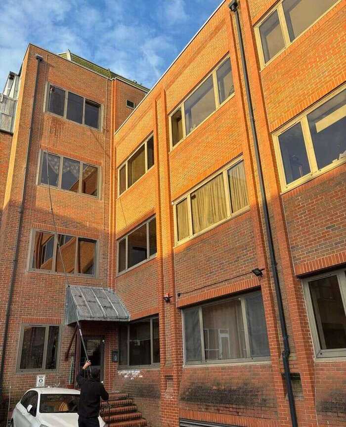 Window cleaner using a long pole on windows of a red-brick building