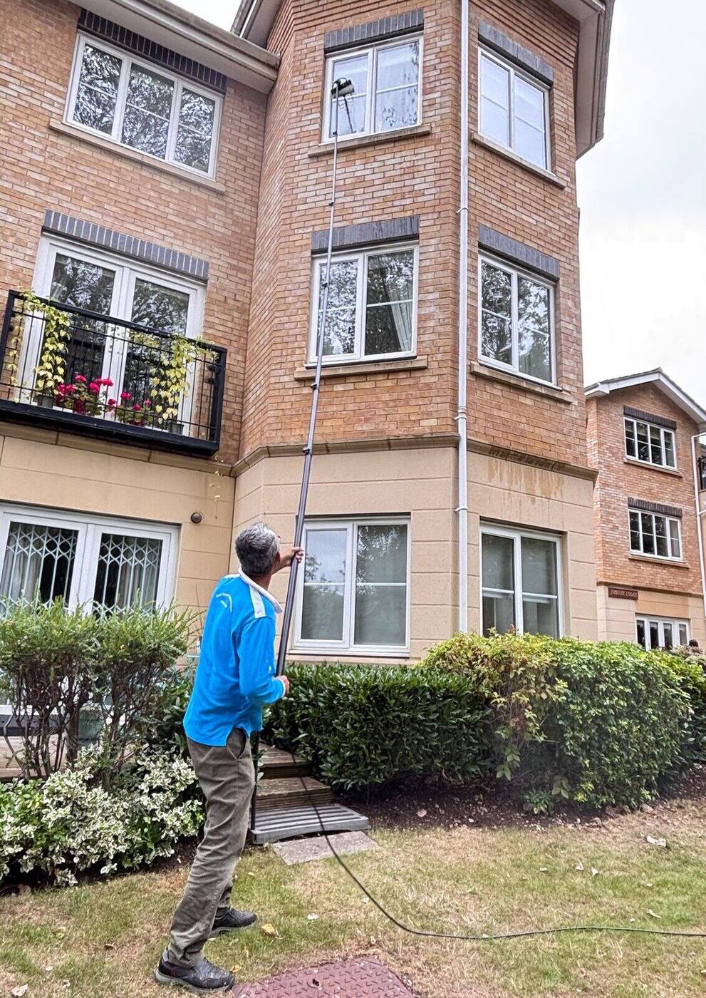 Window cleaner operating a water-fed pole at full extension against the glazing of a commercial building, pole visible from ground to tip