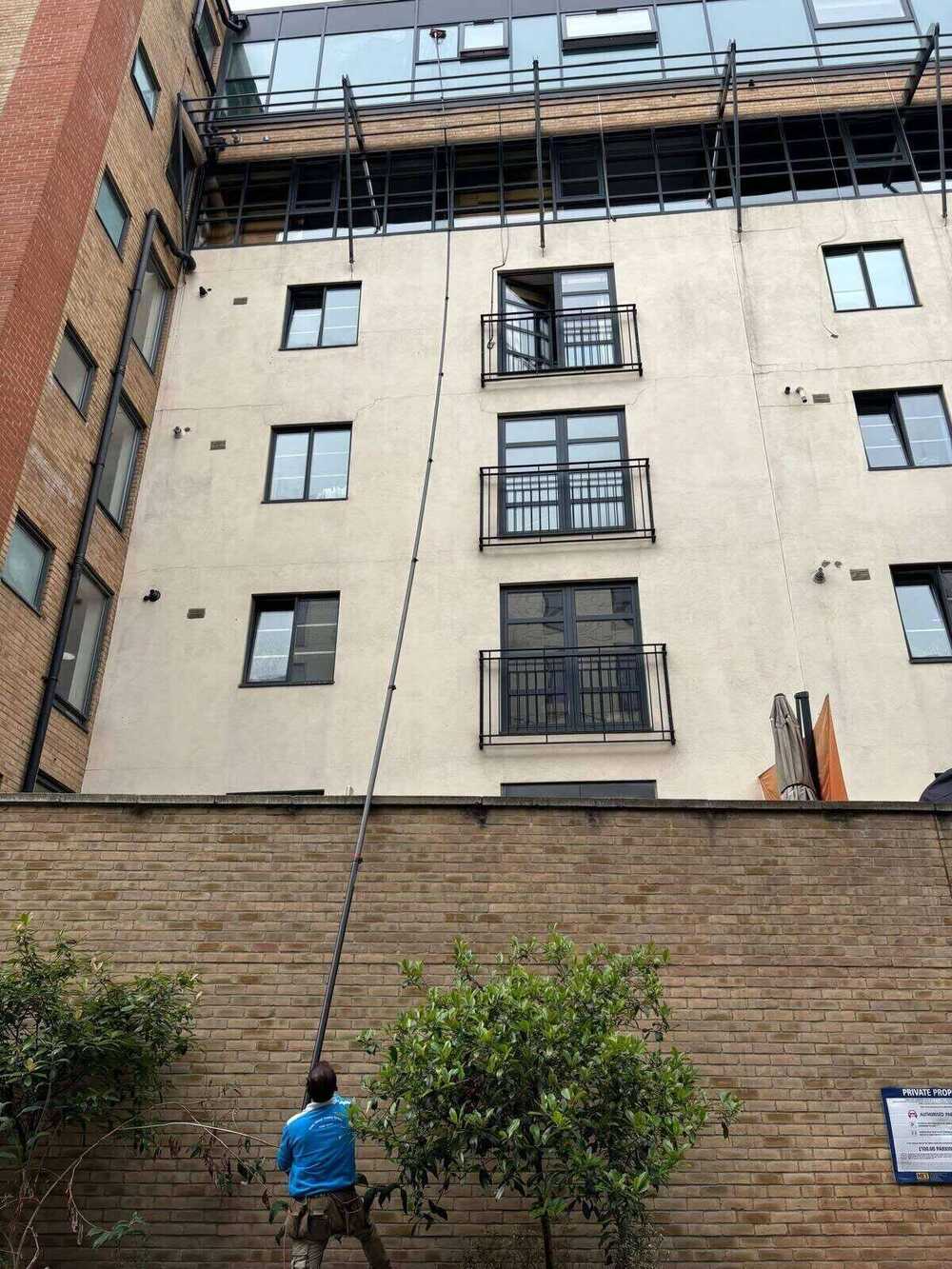 Window cleaner using a water-fed pole at full extension against a tall building
