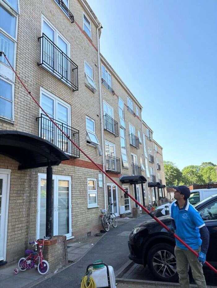 Cleaner using a long pole to reach windows on a modern apartment building