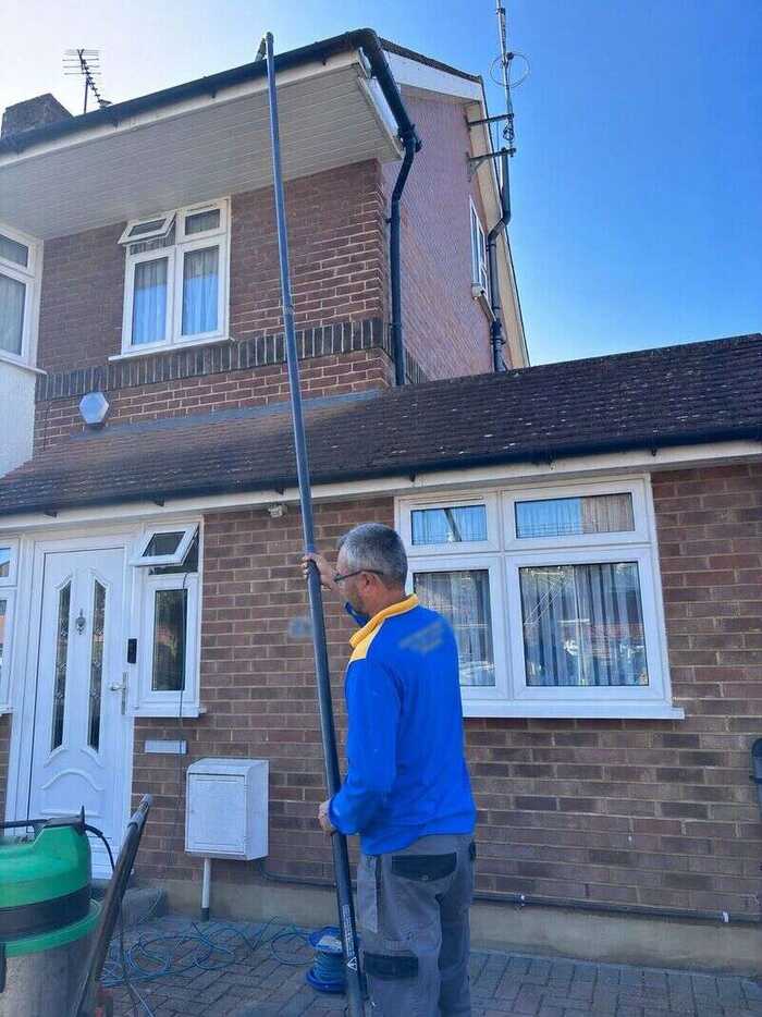 Window cleaner using a long pole on the upper windows of a brick house