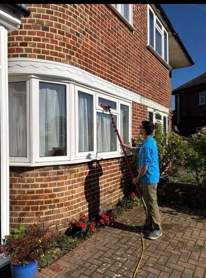 Window cleaner using a water-fed pole on the bay window of a red-brick house