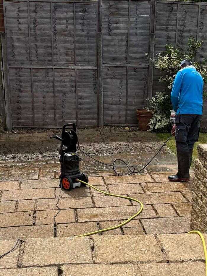 Cleaner pressure washing a paved patio beside a wooden fence