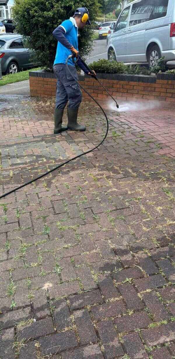 Cleaner pressure washing weeds and dirt from a block-paved driveway