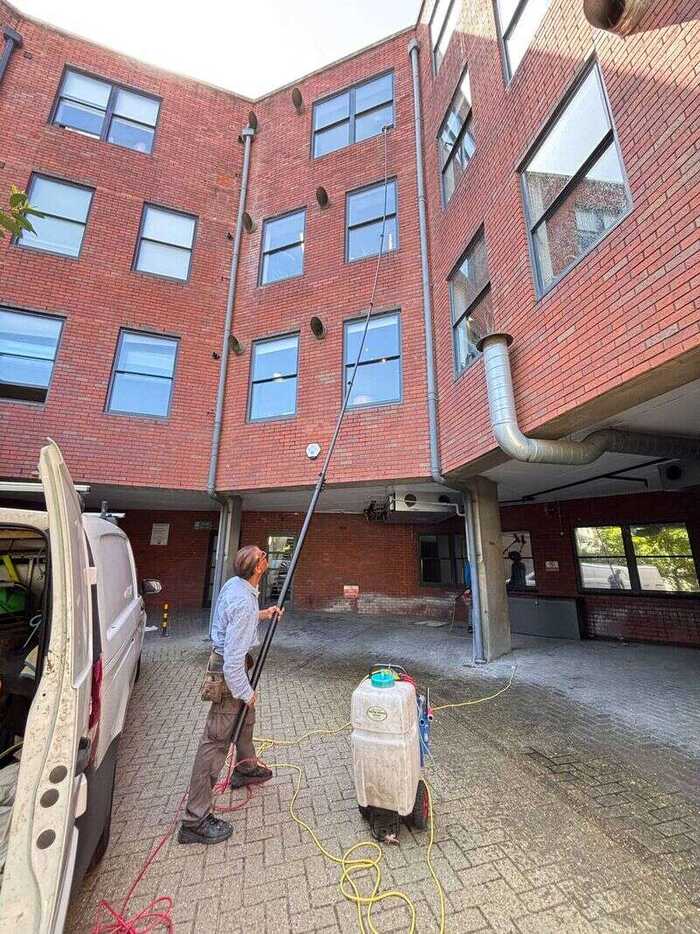 Window cleaner using a long pole on windows of a red-brick apartment building