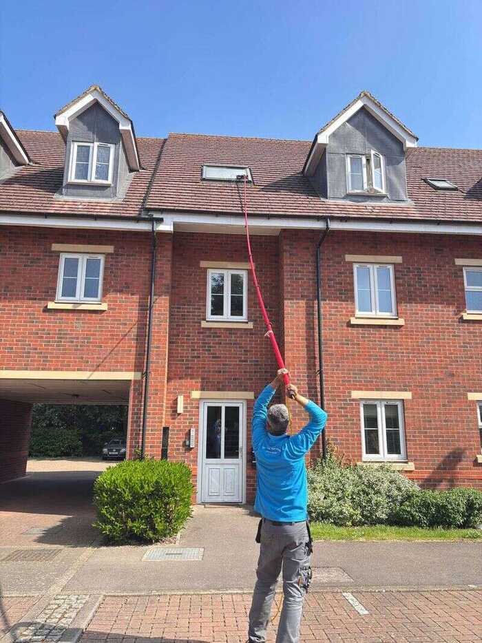 Window cleaner using a long pole on windows of a red-brick building