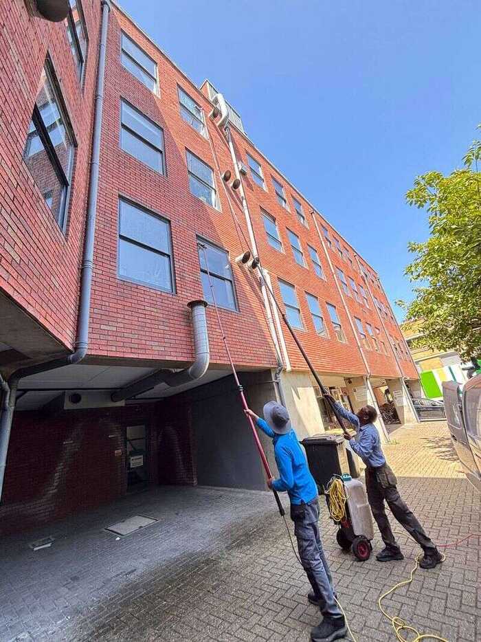 Two window cleaners working on the windows of a multi-storey brick building